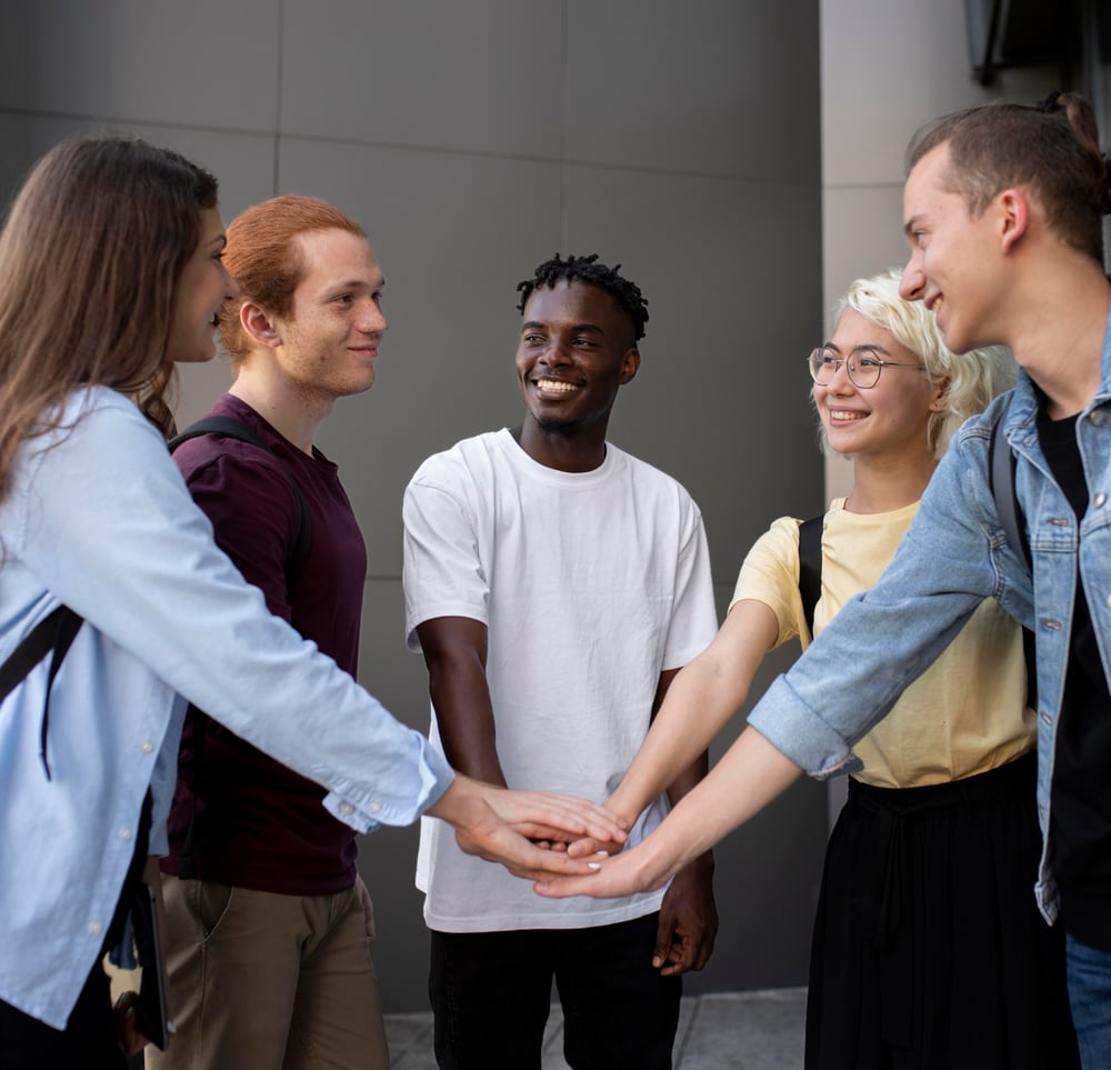 Group of university students from the students’ union stacking their hands in a circle to symbolize teamwork and collaboration